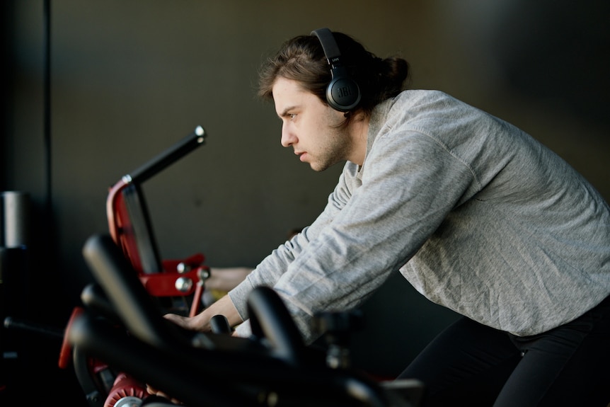 a man with headphones leans while riding an exercise bike