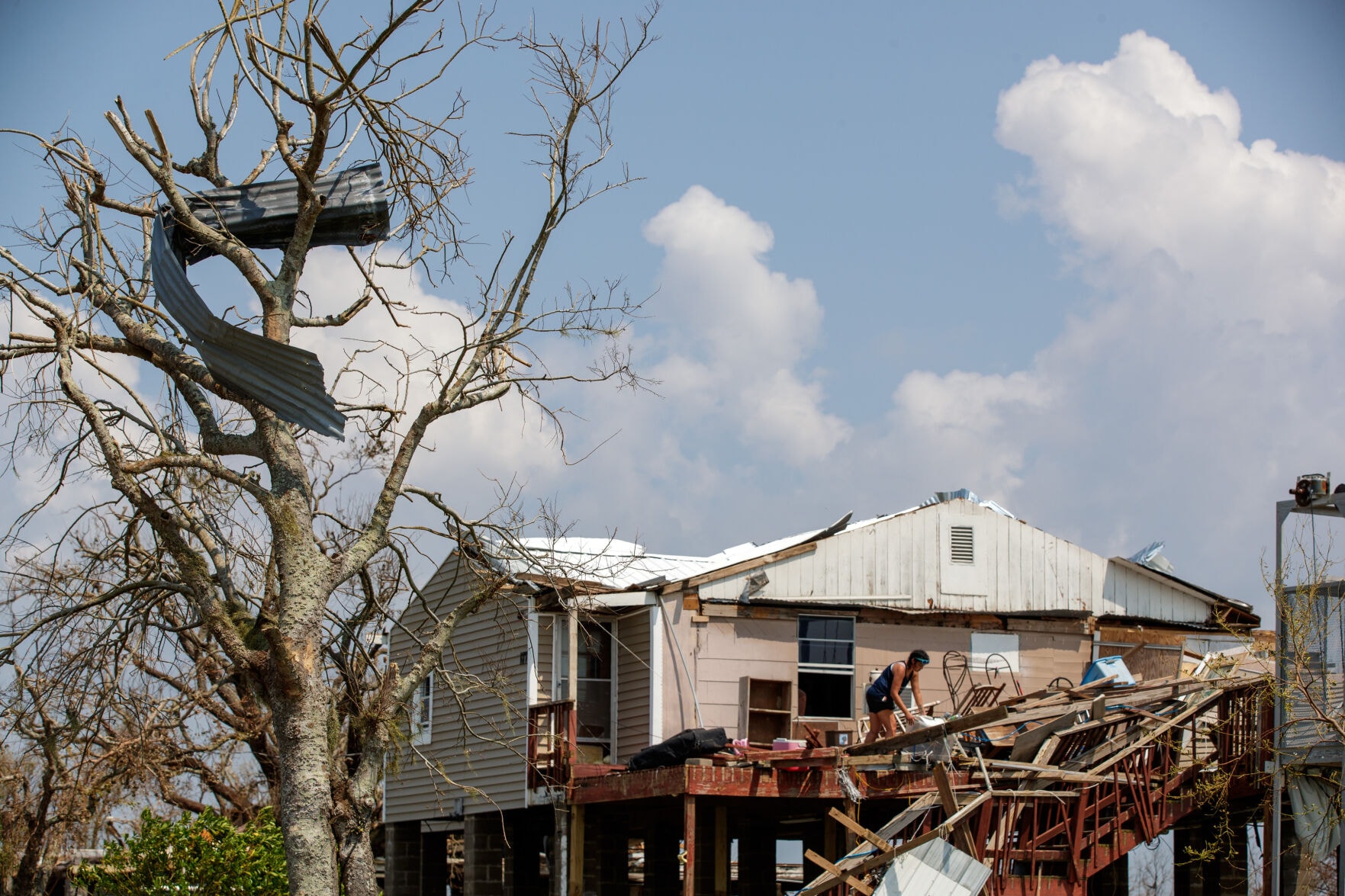 A person stands on the deck of a badly damaged house.