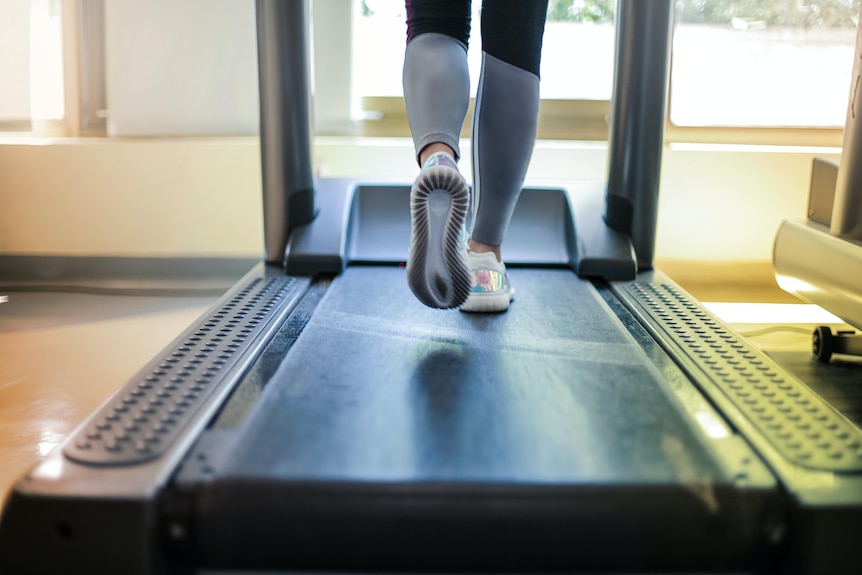 a woman in a black tee swings her arms as she runs on a treadmill